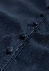 Gros plan sur un tissu bleu foncé avec des boutons ronds recouverts de tissu le long d’une couture cousue.