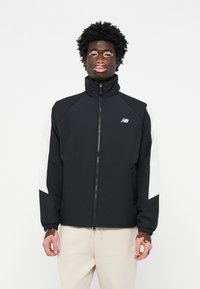 Giacca nera con colletto alto, dettagli bianchi sulle maniche, chiusura con zip e polsini elastici, realizzata in materiale leggero e morbido.