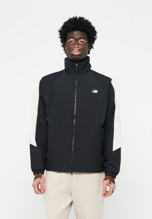 Schwarze Jacke mit hohem Kragen, weißen Akzenten an den Ärmeln, Reißverschluss und elastischen Bündchen, hergestellt aus einem glatten, leichten Material.