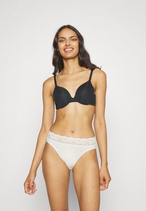 Reggiseno nero senza cuciture con spalline regolabili e finitura liscia, abbinato a slip bianchi con bordo in pizzo. Entrambi hanno un design minimalista.