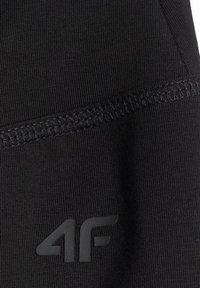 Gros plan sur un tissu noir avec des coutures visibles et un logo de la marque 4F noir mat imprimé sur la partie inférieure.