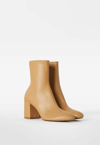 Botines de piel marrón con tacones cuadrados y costuras visibles, mostrados uno al lado del otro sobre un fondo blanco liso.