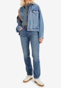 Chaqueta de mezclilla con corte oversize, color azul claro, bolsillos frontales y cierre de botones. Combinada con jeans de pierna recta en un tono a juego y zapatillas blancas.