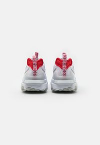 Zapatillas blancas con acentos rojos, parte superior de malla texturizada, suela acolchada y tiradores en la parte trasera para ponerlas y quitarlas fácilmente.