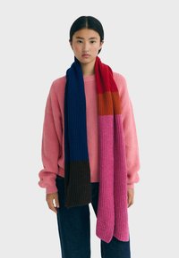 Écharpe en tricot multicolore présentant des rayures bleues, rouges, orange, roses et marron. Texture côtelée, design long.