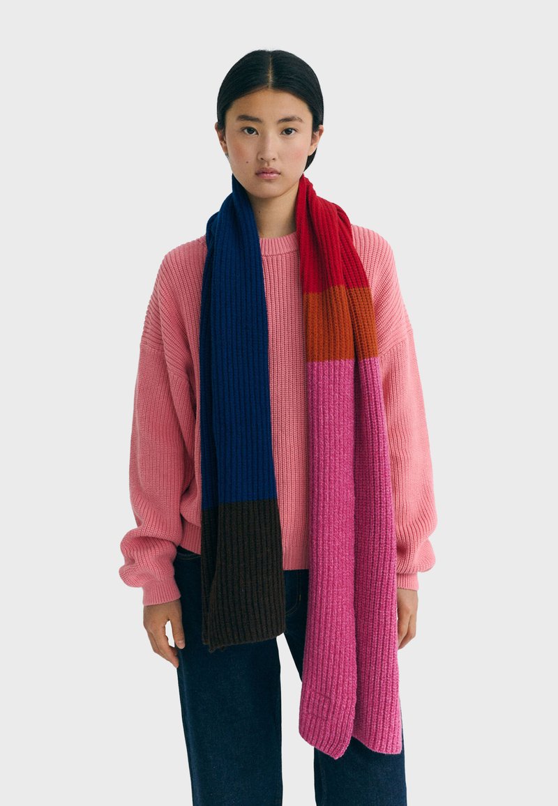 Écharpe en tricot multicolore présentant des rayures bleues, rouges, orange, roses et marron. Texture côtelée, design long.