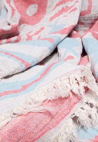 Lightweight fabric with pink and blue abstract floral patterns, woven texture, and decorative fringed edges, softly folded.