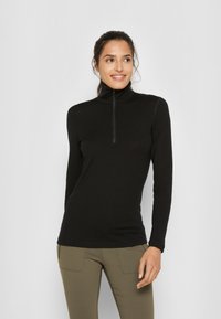 Czarna bluzka z długim rękawem, wysoka stójka i zapięcie na ćwierć zamka. Wykonana z gładkiego, elastycznego materiału, dopasowany krój, połączona z oliwkowymi spodniami.