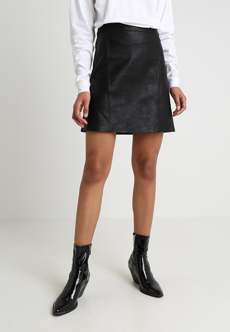 Mini gonna in pelle nera con texture liscia, cuciture frontali e vita aderente. Abbinate a stivali alla caviglia neri lucidi con punta affusolata.
