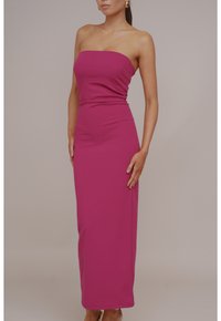 Abito lungo fucsia senza spalline realizzato in tessuto elasticizzato, con un corpetto aderente, dettagli drappeggiati in vita e una texture liscia.