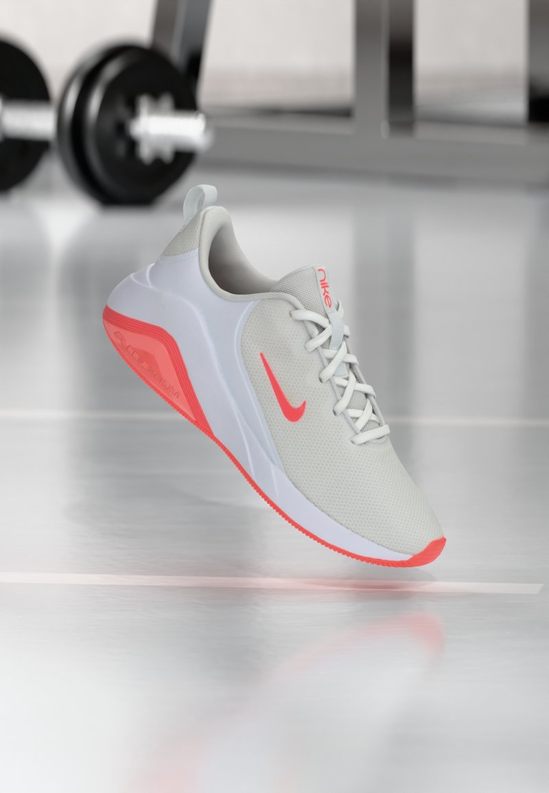 Light gray athletic shoe with a breathable mesh upper, white sole, and vibrant coral accents. Features a lace-up design and padded collar.