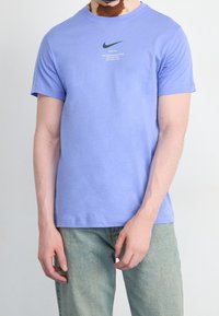 Ljuslila bomullströja med korta ärmar, rund halsringning och svart Nike-logotyptryck på bröstet. Bärs med ljusblå jeans.