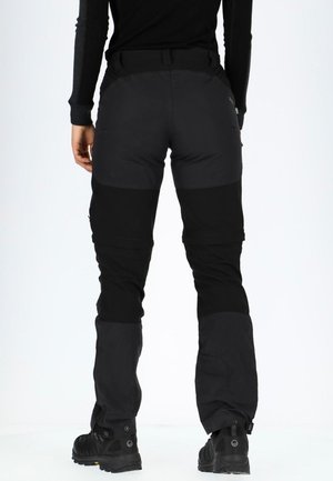 Pantaloni neri da esterno dal design aderente, con pannelli in tessuto a contrasto e polsini regolabili. Abbinati a calzature robuste nere.