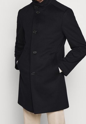 Marineblauwe wollen blendjac met een hoge kraag, zes knopen aan de voorkant, zijzakken en een gestructureerde pasvorm. Glad textuur met minimale details.