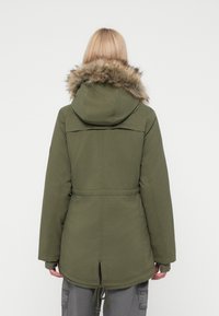 Olive roheline parka, millel on kunstkarusnahast voodriga kapuuts, elastne vöökoht ja reguleeritav pehme detail. Omaduseks on pikem seljaosa ja kõrvaribad.