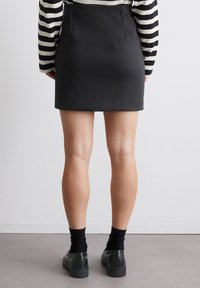 Gonna nera aderente con pences sul retro, abbinata a scarpe scure e calze nere; sopra si vede una maglietta a righe crema e nere con maniche lunghe.