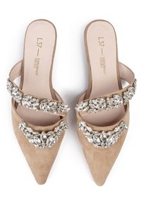 Beige mockasiner i suedepäls med spetsig tå och dubbla kristallprydda remmar över toppen, med en slät innersula och platt sula.