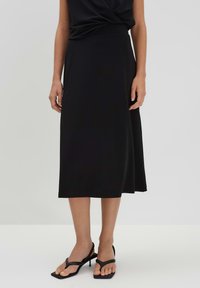 Jupe midi noire en tissu lisse, présentant une silhouette fluide et une taille élastique, associée à des sandales à talons à lanières noires.