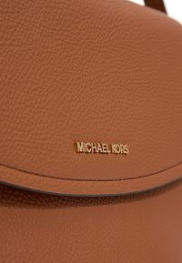Borsa a tracolla in pelle marrone texturizzata con una placca del logo dorata. Presenta un cappuccio arrotondato e una tracolla robusta per il trasporto.