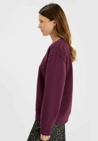 Burgundy sweatshirt with long sleeves, ribbed cuffs and hem, featuring a round neckline and a relaxed fit, paired with a leopard print skirt.