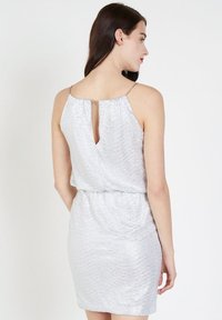 Vestido de lentejuelas plateadas con una textura en forma de concha, que presenta un escote en la parte baja de la espalda y finas tirantes. Silueta ajustada.