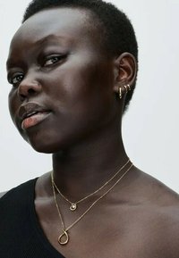 Goldschmuck umfasst mehrere zarte Halsketten in unterschiedlichen Längen, die einen kleinen runden Anhänger und einen einzigartigen tropfenförmigen Charme tragen.
