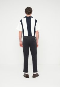 Polo à manches courtes avec rayures verticales bleu marine et blanches, doté d'un col plat. Associé à un pantalon foncé et des chaussures marron.