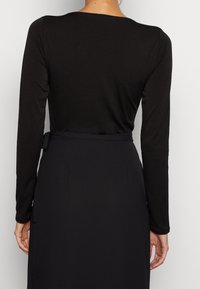 Zwarte lange mouwen top met een ronde halslijn, met een gladde textuur en een getailleerd ontwerp, gecombineerd met een hoge taille zwarte rok met strikdetail.