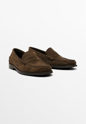 Mocassins en daim marron avec un design de style mocassin, comportant des détails cousus et un petit talon. Texture lisse avec une silhouette classique.