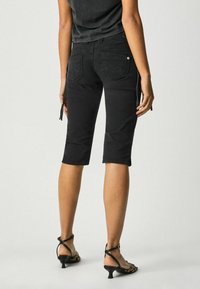 Vaqueros negros cortos con un diseño ajustado, dos bolsillos traseros y costuras decorativas. Combinados con tacones negros con tiras.