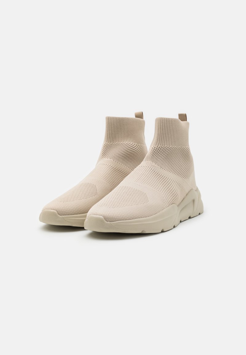 Baskets style chaussettes beige avec une tige en tricot texturé et une semelle en caoutchouc flexible. Comprend une languette à l'arrière.
