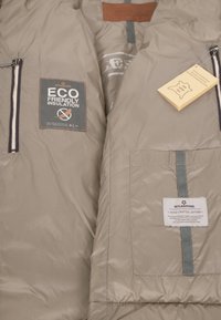 Beige isolierte Weste aus glattem Stoff, mit umweltfreundlichen Isolierungsschilden, Lederakzenten und vorderen Reißverschlusstaschen.