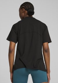 Zwarte korte mouwen t-shirt gemaakt van gladde stof, met een gebogen schoudernaad over de achterkant en een losse pasvorm. Gecombineerd met blauwe shorts.