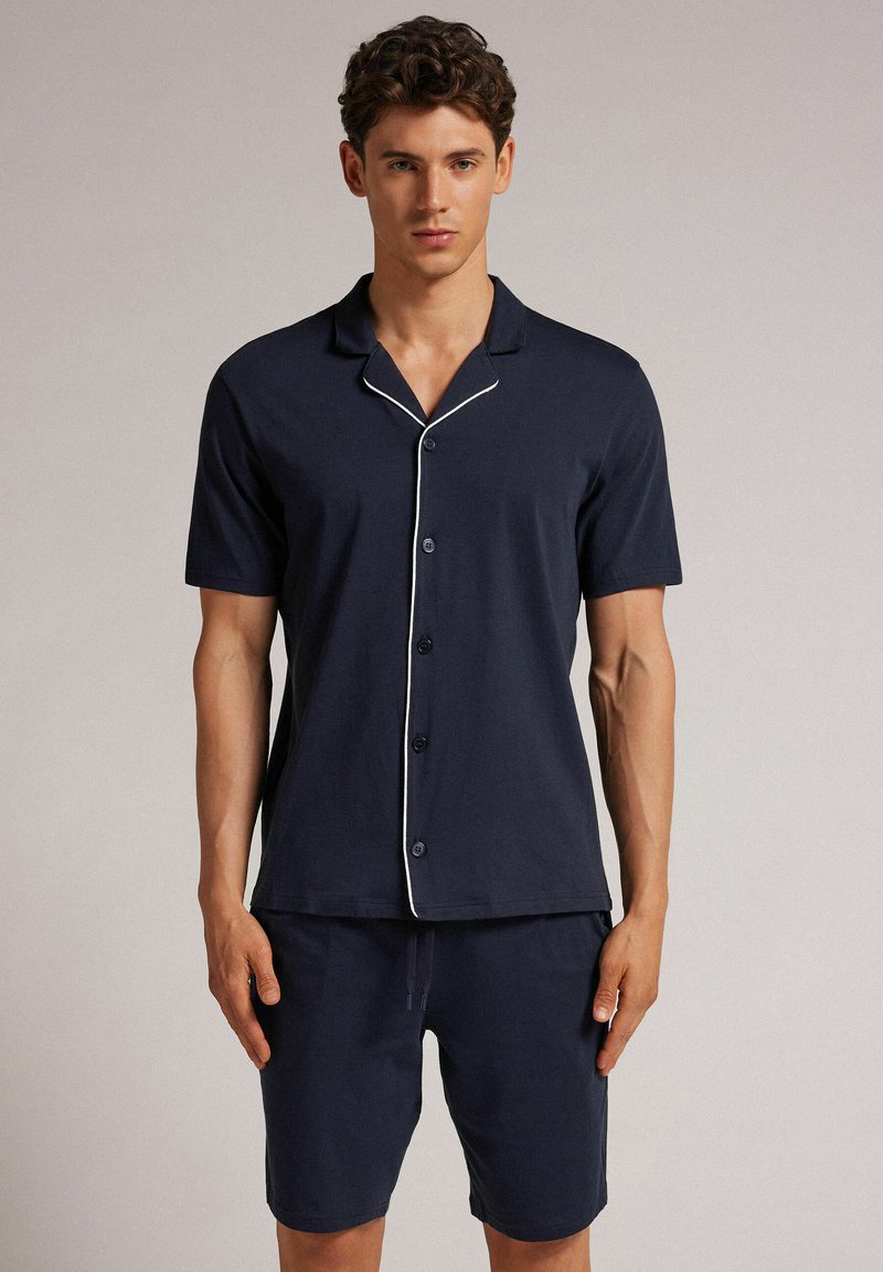 Conjunto de pijama de hombre en color navy de manga corta, fabricado con tela suave; cuenta con cierre de botones, cuello con muesca y detalles en blanco en las paredes de la camiseta.