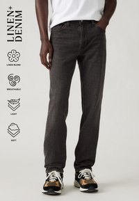 Fekete vászonkeverék farmernadrág egyenes szabású, finom textúrával, öt zsebes kialakítással, amit színes sneakers-cipőkkel párosítottak.