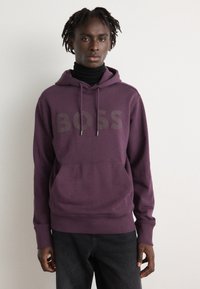 Lila Kapuzenpullover mit einem großen "BOSS"-Logo in Dunkelgrau. Verfügt über eine vordere Kängurutasche und gerippte Bündchen, hergestellt aus Baumwollmischgewebe.
