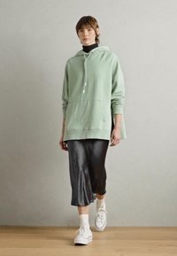Mintgroene hoodie met een grote voorkant zak, gecombineerd met een zwarte coltrui, een grijze midi skirt en witte sneakers. Glad textuur, ontspannen pasvorm.