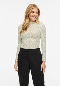 Top verde chiaro in pizzo a maniche lunghe con motivo floreale, abbinato a pantaloni neri a vita alta. Tessuto liscio, vestibilità slim, scollo tondo.