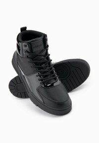 Černé vysoké tenisky vyrobené z kůže a syntetických materiálů, kulatá špička, šněrovací design, texturovaná podrážka a značka na jazyku.