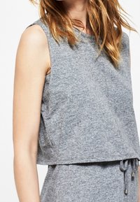 Crop top gris sans manches en tissu doux avec une coupe décontractée, doté d'un col rond et d'une texture chinée subtile.