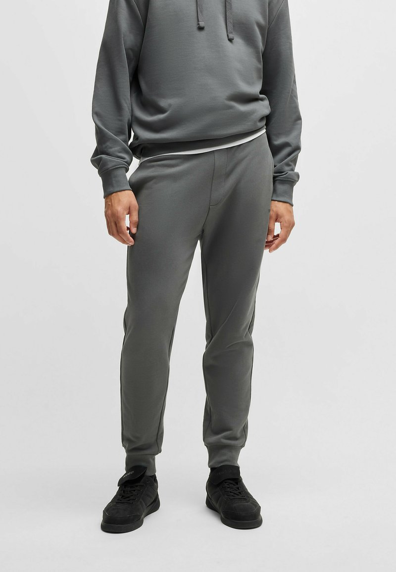 Grijze sweatpants en bijpassende hoodie, gemaakt van zacht materiaal. Slim fit ontwerp met ribbels aan de manchetten, voorzien van een verstelbare capuchon met koord.