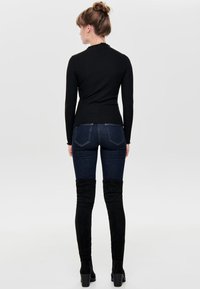 Langmouw zwart ribbeltop gecombineerd met donkerblauwe skinny jeans en hoge zwarte suède laarzen, wat een nauwsluitende silhouet laat zien.
