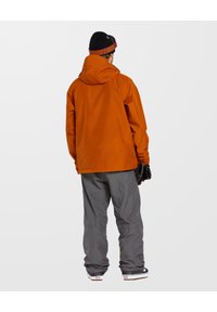 Orange vandtæt jakke med hætte, parret med grå snebukser. Sættet inkluderer sorte handsker og sko med hvid sål.