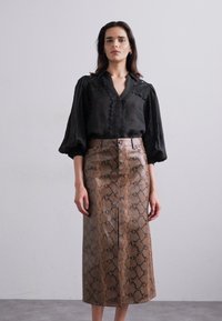 Zwarte blouse met knopen en pofmouwen, gecombineerd met een middellange bruine rok met slangenprint en een vooruitsnijding, met een soepele textuur.
