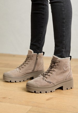 Bottes cheville en daim beige avec une finition texturée, design à lacets, fermeture éclair latérale et semelle épaisse en caoutchouc. La doublure de la botte est douce et moelleuse.