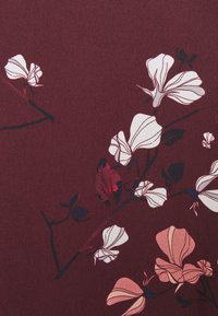 Tessuto color bordeaux con un motivo floreale di fiori bianchi e rosa pallido, foglie verde scuro e sottili accenti lucidi.