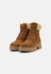 Botas de ante marrón hasta el tobillo con un cuello de textura suave y esponjosa, puntera redondeada y suela de goma beige gruesa. Cuenta con cordones para un ajuste seguro.