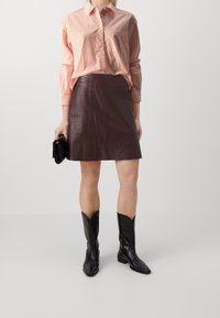 Woman wearing a red and white striped shirt tucked into a brown leather skirt, holding a black clutch, and wearing black cowboy boots.