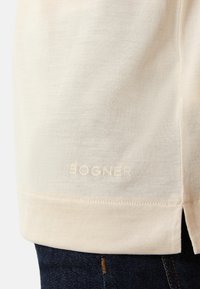 Cremefarvet kortærmet skjorte lavet af blødt stof, med en syet kant og sideslids, samt et subtilt "BOGNER" logo nederst.