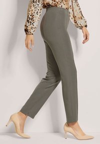 Olijfgroene, op maat gemaakte broek met een slim fit, enkel-lange zoom en zijsplitten. Gepaard met beige high-heel pumps.